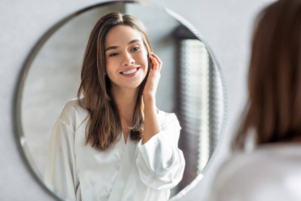 Beauty,Concept.,Portrait,Of,Attractive,Happy,Woman,Looking,At,Mirror Woman smiling in the mirror after a midface lift procedure in Newport Beach, CA